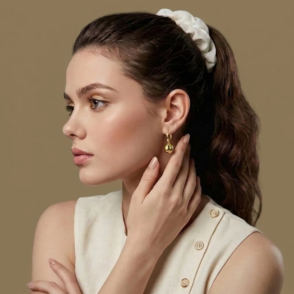 Woman wearing gold earrings with a beige background