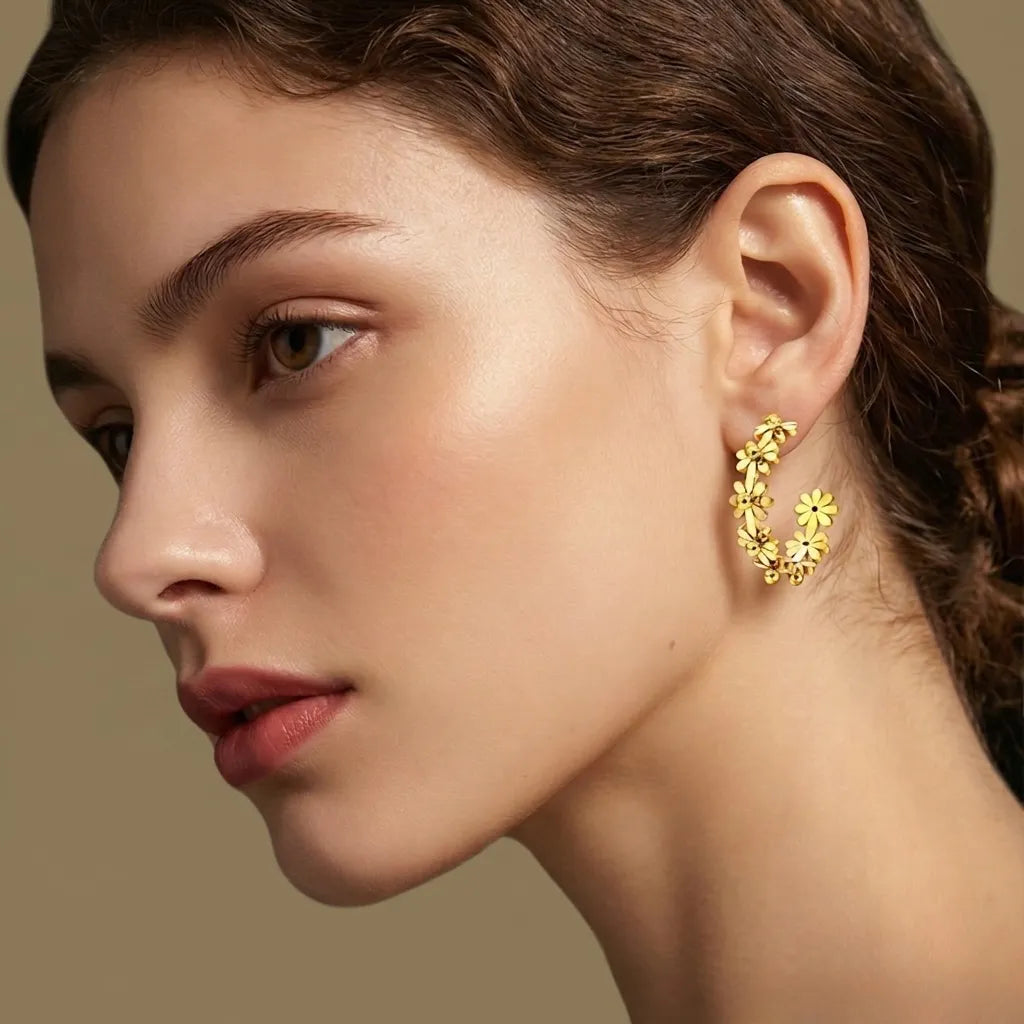 Close-up of a woman wearing gold hoop earrings with floral details on a neutral background