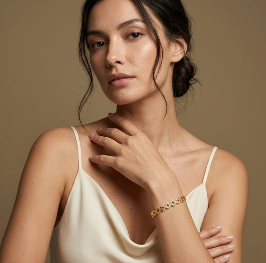 Woman wearing a cream top and gold round bracelet against a brown background