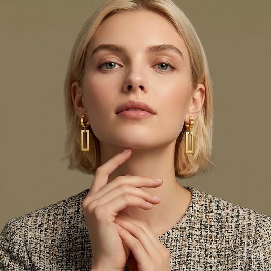 Woman wearing rectangle gold earrings with a neutral background
