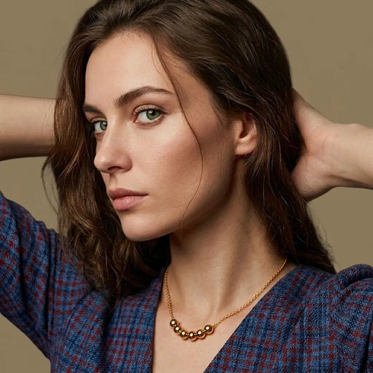 Woman with hands in hair wearing a blue patterned top and gold necklace against a beige background